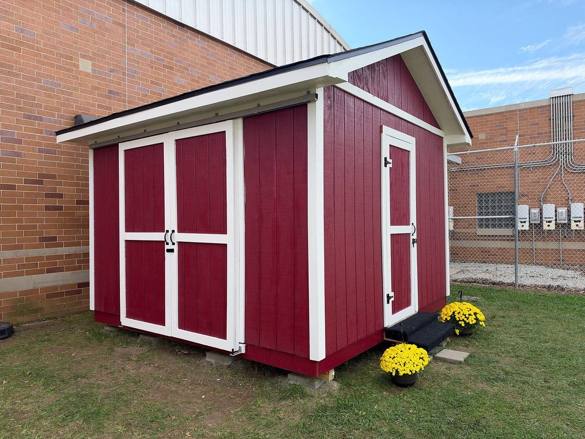 The finished 12 by 12 red shed with white trim that Foundations participants designed and built, with yellow mums at the door